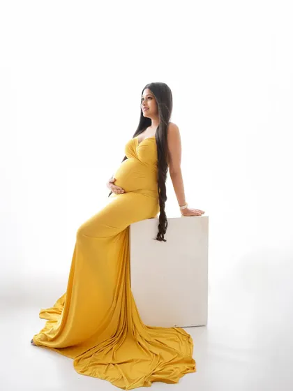 A minimalist and elegant portrait. The focus is on the beautiful silhouette of the mom-to-be in a yellow gown, seated against a clean white background.