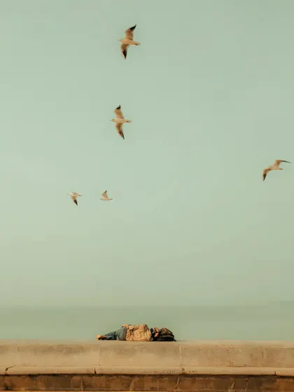 A person lies on the sea wall at Marine Drive, with seagulls flying overhead. This minimalist composition captures a moment of complete relaxation and surrender to the city's seaside atmosphere.