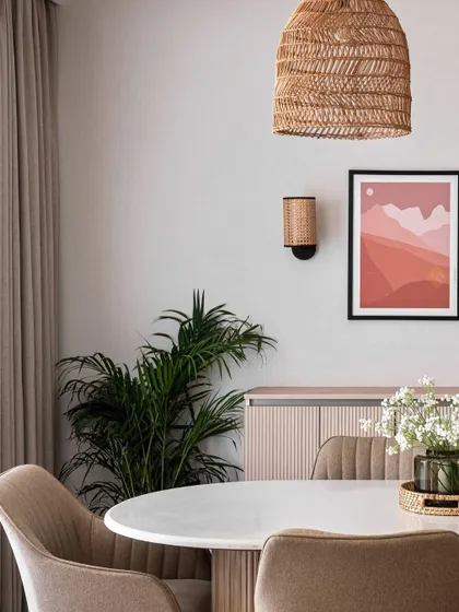 A detail shot of the dining area, featuring a round marble-top table, comfortable upholstered chairs, and modern art. The woven pendant and wall sconces provide warm, layered lighting.