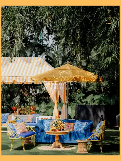 A vibrant lounge setting with a royal blue sofa, bright yellow chairs, and patterned cushions, perfect for a fun and colorful Mehendi.