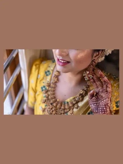 A candid close-up of a bride in a yellow saree, highlighting her beautiful temple jewelry necklace and mehendi.