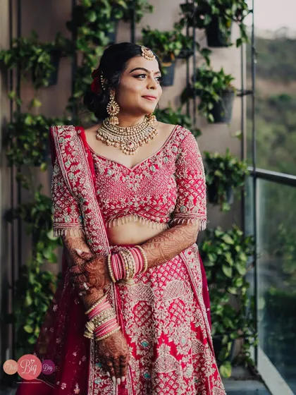 A beautiful portrait of Rucha in her pink lehenga, looking out from a balcony with a natural, green background.