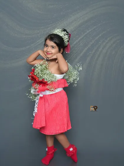 A young girl in a creative floral outfit smiles for the camera. The dress, made of real flowers, is a unique and artistic concept for a portrait session.
