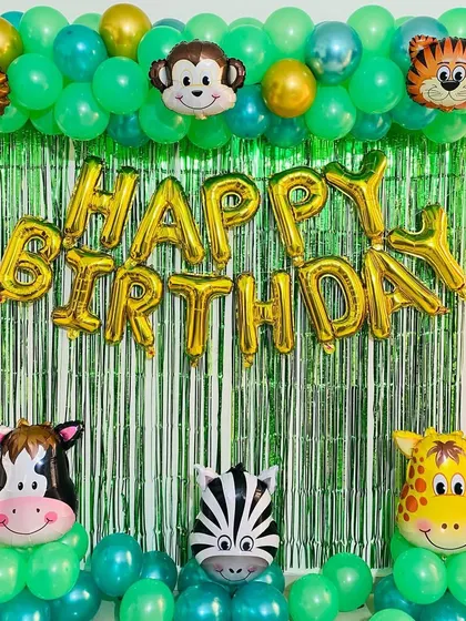 A jungle-themed birthday party with a green foil curtain backdrop. The setup includes a balloon arch and large animal head foil balloons.