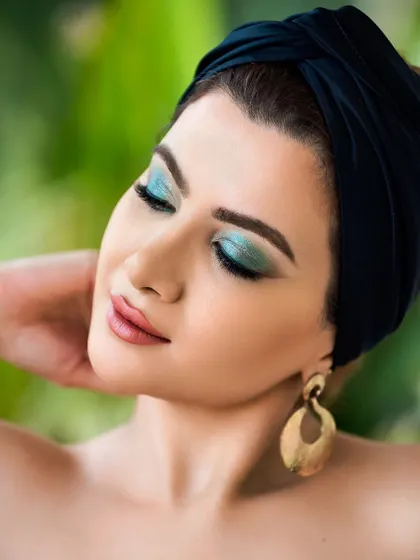 A beauty shot featuring vibrant turquoise eyeshadow, complemented by a black turban and gold earrings. The composition and color palette create a chic and classy portrait.