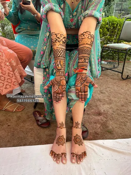 A beautiful shot of a bride showcasing her full hand and foot mehndi. The arm design features classic peacock and floral work, while the feet have elegant mandala patterns.