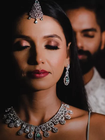 A close-up, artistic portrait focusing on the bride's serene expression, with the groom softly blurred in the background.