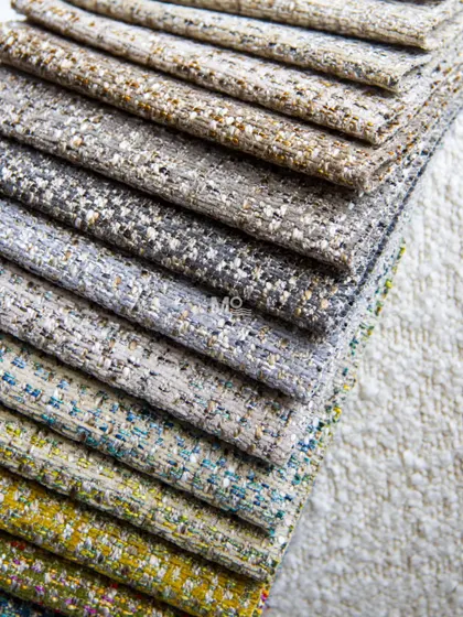 A stack of our textured bouclé fabrics in a range of colors, from earthy neutrals to vibrant yellows and blues. This material adds depth and character to any space.