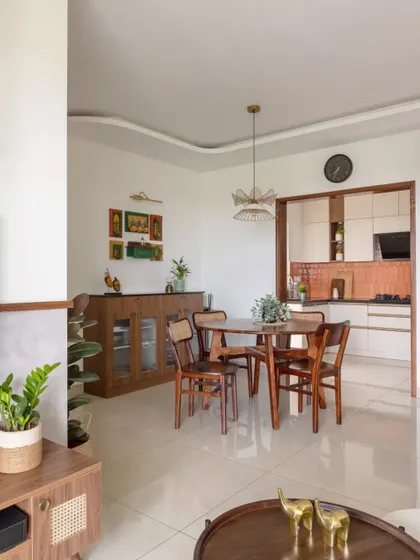 An open-plan living and dining area where classic charm meets modern comfort. The space features a round wooden dining table and a wicker-front TV unit.