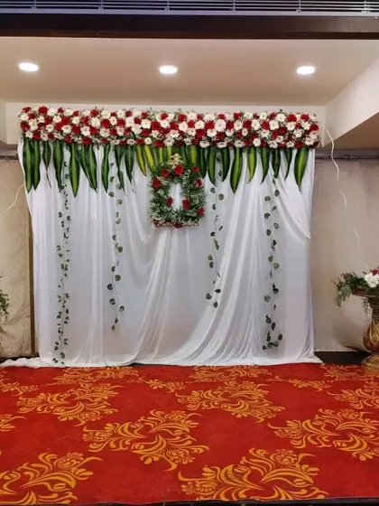 A chic and modern engagement backdrop with a white curtain, a floral wreath, and arrangements of red and white roses. The white bicycle prop adds a whimsical touch.