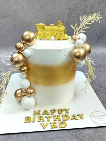 A stylish gold and white train engine cake. This elegant design is decorated with gold and white spheres and dried botanicals.