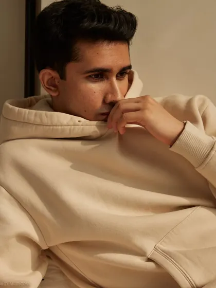 A relaxed and introspective portrait of an actor. The warm, neutral tones of the hoodie and the soft lighting create a comfortable and authentic atmosphere.
