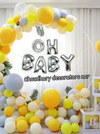 A cheerful "Oh Baby" decoration with a yellow, white, and grey balloon arch, "BABY" blocks, and sunflower accents.