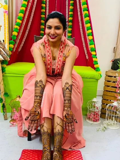 A happy bride displaying her full bridal mehndi. The designs on her hands and feet are intricate and perfectly matched for her wedding day.