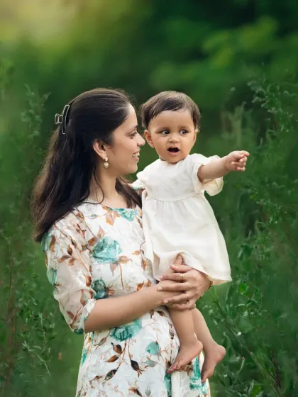 A mother holds her baby girl, who is pointing at something with wonder. This candid moment was captured during a beautiful outdoor sitter session.