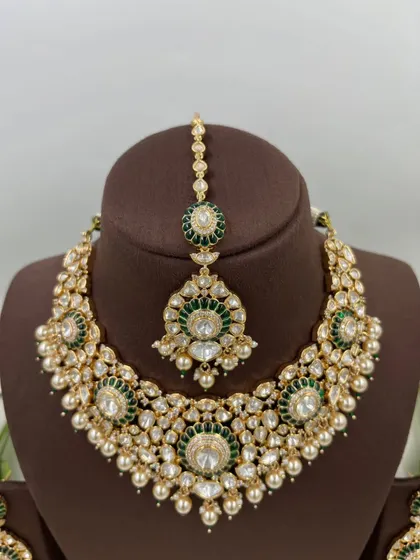 The Zarista Premium Moissanite Necklace set, shown here in both ruby and green variations. This set includes a necklace, maang tikka, and earrings, featuring large central stones surrounded by detailed craftsmanship.