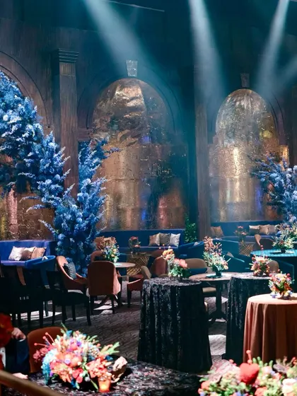 Spotlights cut through the haze, highlighting the dramatic blue florals and creating a moody, theatrical atmosphere.