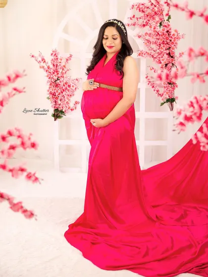 This full-length portrait showcases the beautiful drape of the pink satin gown against a soft, floral backdrop. The tiara adds a touch of regal elegance.