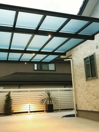 This modern carport features a translucent polycarbonate roof and a minimalist black frame. The design provides shelter for the vehicle while allowing light to pass through, preventing the area from feeling dark.