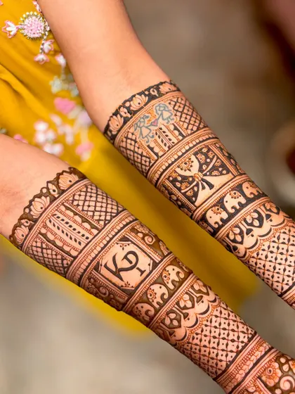A close-up of the forearm bands from Kavitha's wedding mehendi, showing the "KP" initials and butterfly motifs.