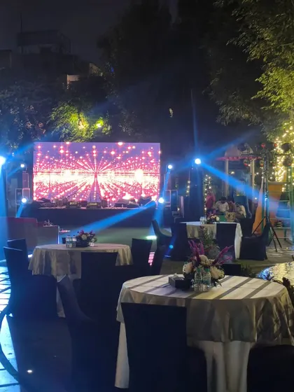 The outdoor seating area for a Diwali night event, with tables, a large LED screen, and trees wrapped in fairy lights.