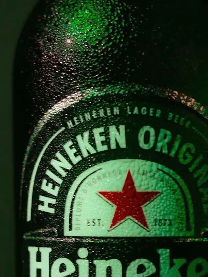 A macro shot focusing on the iconic Heineken label, with detailed condensation on the green glass. This close-up highlights the branding and texture of the product.