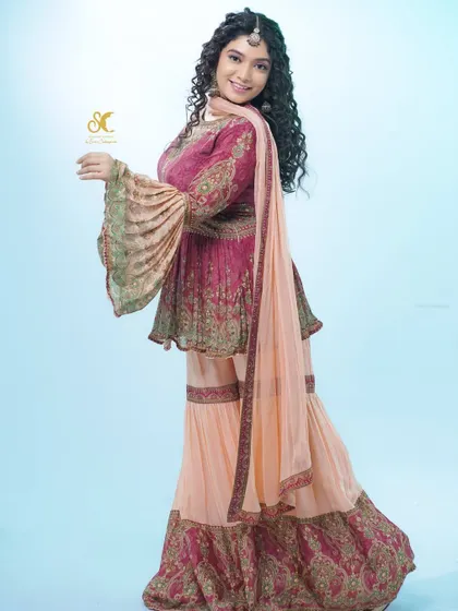 The gorgeous actress Priyanka Thimmesh in a stunning sharara set. The outfit features a magenta peplum-style kurta with bell sleeves and heavy embroidery, paired with contrasting peach sharara pants.