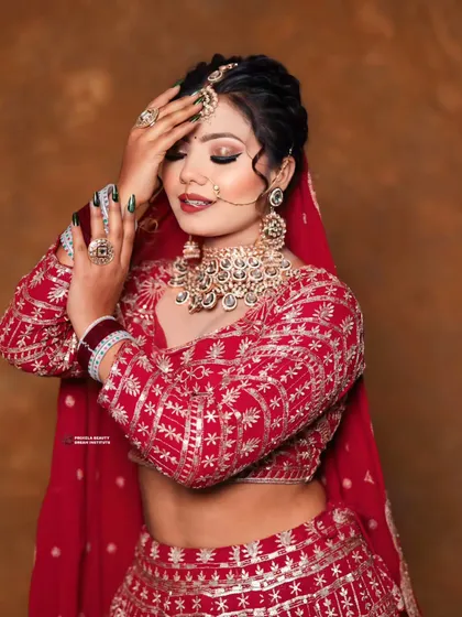 A stunning bridal look focusing on the soft glam makeup and the elegant updo. The bride's nails, a deep emerald green, offer a modern and unexpected contrast to her red lehenga.