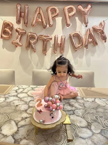 The birthday girl sitting by her cake in her custom pink tulle dress. The layered skirt creates a lovely, full shape that's perfect for party photos.