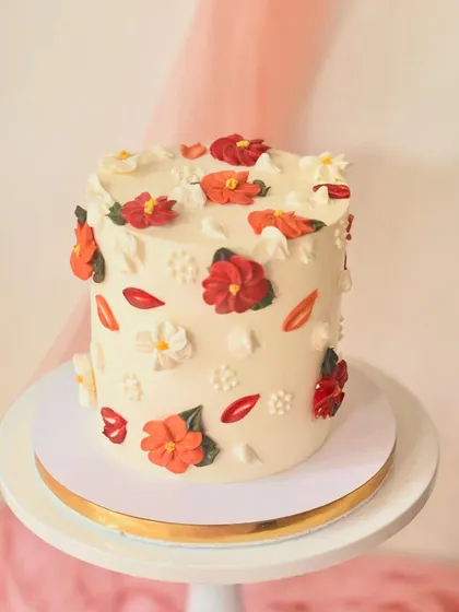 A lovely tall cake decorated with simple, stylized piped flowers in red and orange hues. The scattered design gives it a fresh and modern botanical look.