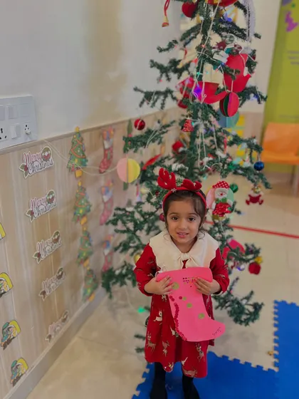 A proud girl holds up her handmade Christmas stocking in front of the tree.