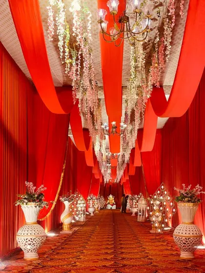 This entrance features a ceiling of hanging floral strings under red fabric drapes, adding a delicate and romantic touch to the walkway.