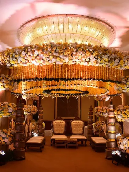The full view of the yellow and white marigold mandap, showcasing its grand scale within the ballroom. The design features ornate seating for the couple and pillars adorned with floral arrangements.