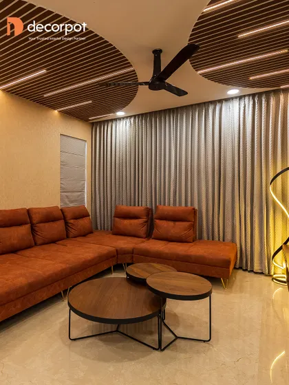 This living room makes a bold statement with its rust-colored sofa and dramatic ceiling design. The TV unit is kept simple and low-profile to balance the other strong elements in the room.