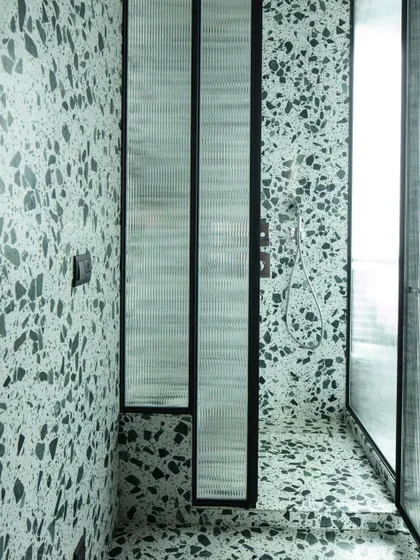 The shower area is defined by fluted glass panels, which provide privacy while allowing light to filter through, maintaining the bathroom's bright and airy feel.