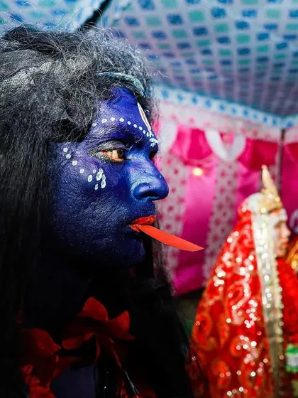 A performer at Bengal's Gajan festival, painted blue and in character. The image captures a quiet moment of preparation before the energetic dance begins.