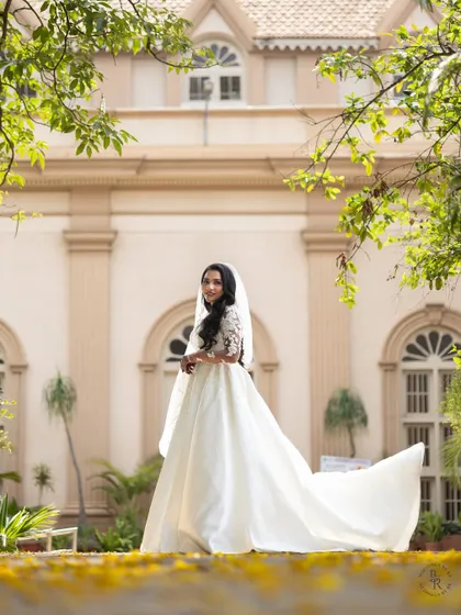 A bride in her beautiful white wedding gown, captured in a garden setting. The framing with natural foliage adds a soft, romantic touch to this elegant portrait.