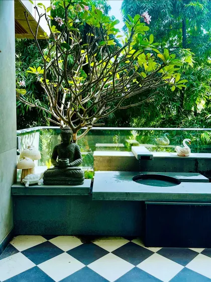 A stunning balcony water feature in Swami Nagar, Delhi. The design includes a gentle fountain, a Buddha statue for serenity, and a beautiful Frangipani tree, all set against a backdrop of lush greenery.