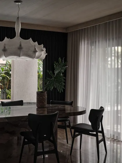 A close-up of the dining area, showing the contrast between the heavy marble table and the delicate, flowing sheer curtains. The space feels both grounded and light.