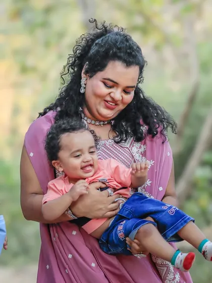 A mother holds her laughing baby boy in her arms, her face glowing with happiness. This candid shot captures the pure joy of motherhood during a relaxed outdoor family session.