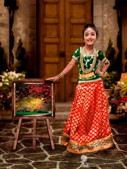 A young girl in a gorgeous green and red traditional lehenga, posing like a little artist with her painting on an easel. This concept blends cultural elegance with creative fun.
