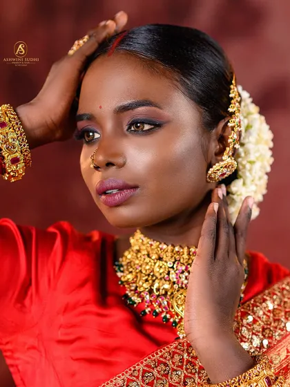 A close-up portrait showcasing the artistry of South Indian bridal styling. The focus is on the traditional jasmine flowers in the hair, the gold jhumkas, and the dramatic eye makeup.