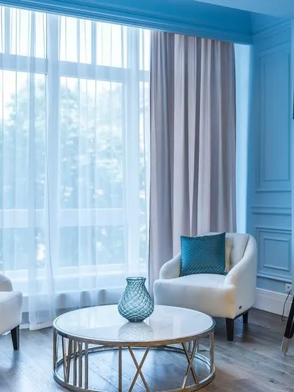 A chic seating nook within the blue-themed living room. Two modern white armchairs are paired with a marble-top coffee table and a dramatic, large-scale tripod floor lamp.