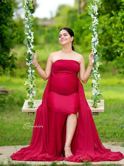 A serene and joyful portrait of a mother-to-be in a flowing red gown, seated on our floral swing. This setup in our private garden is perfect for capturing relaxed, candid moments that radiate happiness.