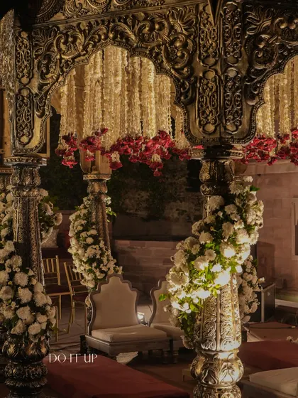 A detail shot of the mandap's carved pillars, wrapped in spirals of white chrysanthemums. This technique adds softness and texture to the metal structure, blending strength with romance.
