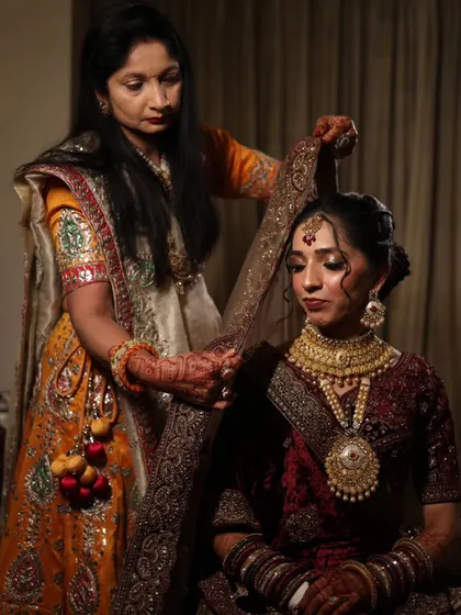 A precious moment as the bride gets her dupatta set. Her makeup features a classic bridal glow with defined eyes and a bold lip.