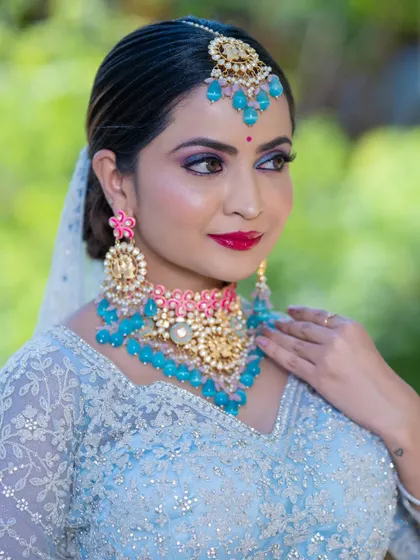 This bride is a vision in a powder blue lehenga with intricate silver work. The makeup features a bold pink lip and smoky eyes, complemented by stunning turquoise and pink jewelry.