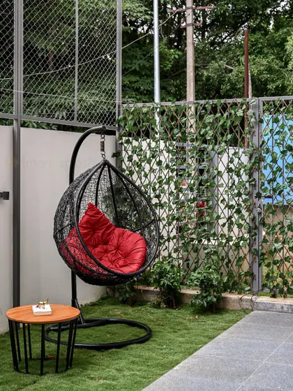 This simple outdoor seating area features a comfortable egg-shaped swing chair with a bright red cushion, set in a garden with a vertical ivy screen.