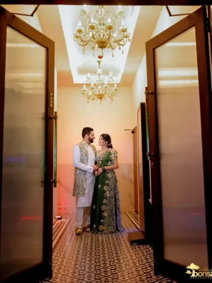 A grand shot of the couple framed by a doorway, with a beautiful chandelier overhead.