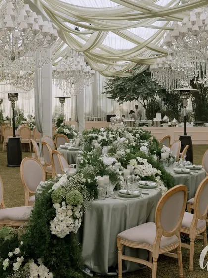 An example of our classic and timeless reception design, this 'Ivory Garden' theme features a stunning floral runner cascading down a long guest table. The space is illuminated by magnificent crystal chandeliers, blending natural elegance with sophisticated glamour.